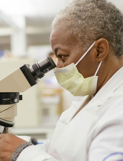 Colleague in lab coat looking into microscope