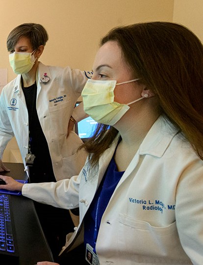 Two MSK colleagues in lab coats looking at mulitple computur screens with X ray information